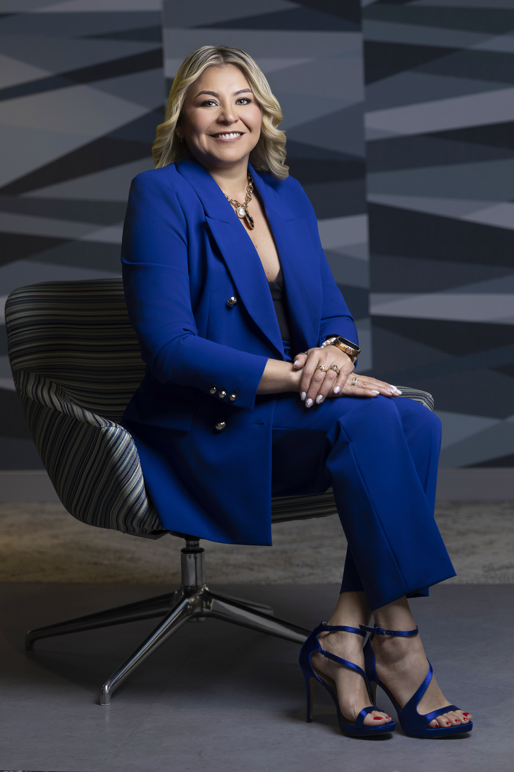 Preparadora de formularios de AC Forms Assistance sonriendo, con traje azul y sentada en un sillón moderno